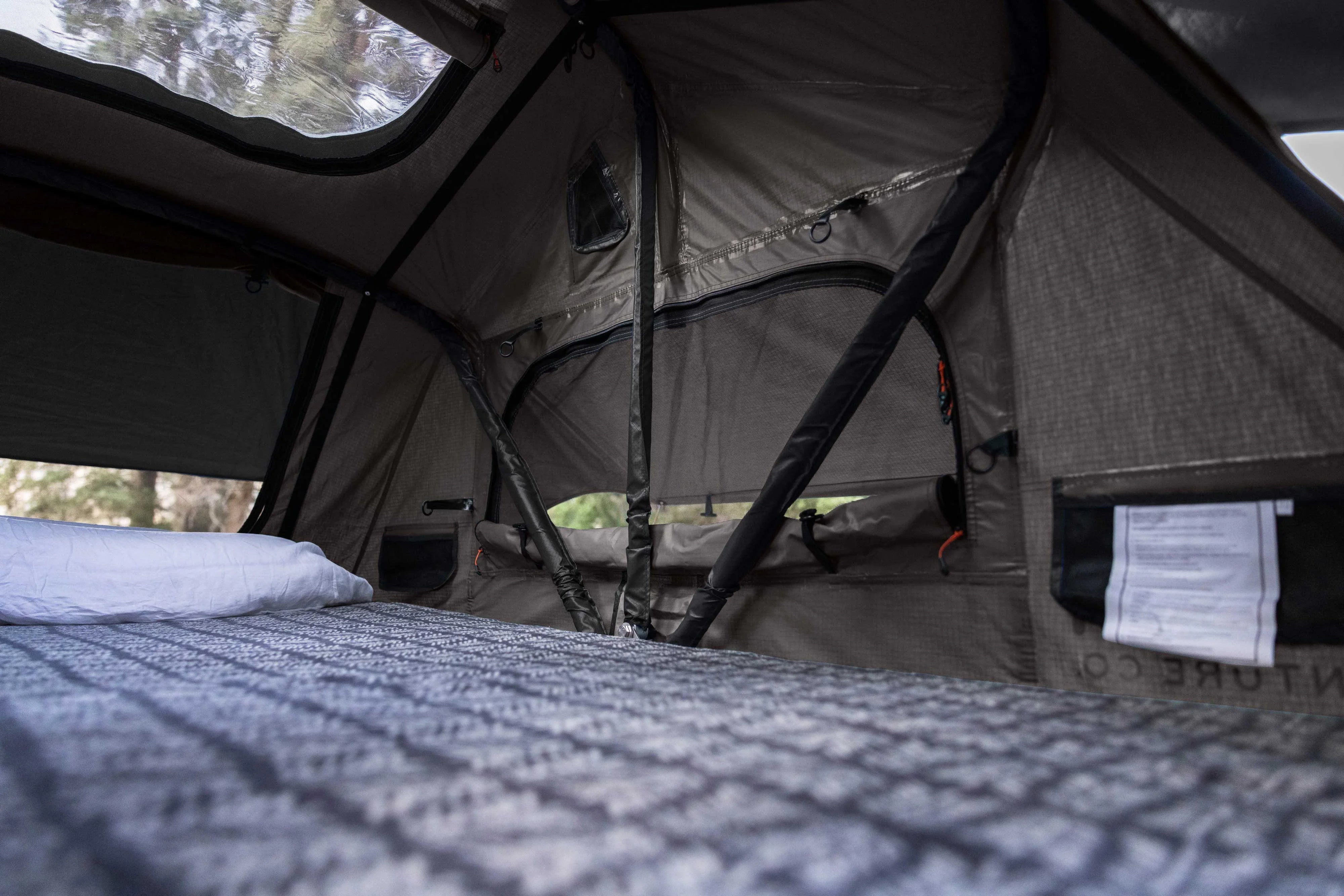 Interior of rooftop tent with bed, mesh windows, and camping gear storage pockets