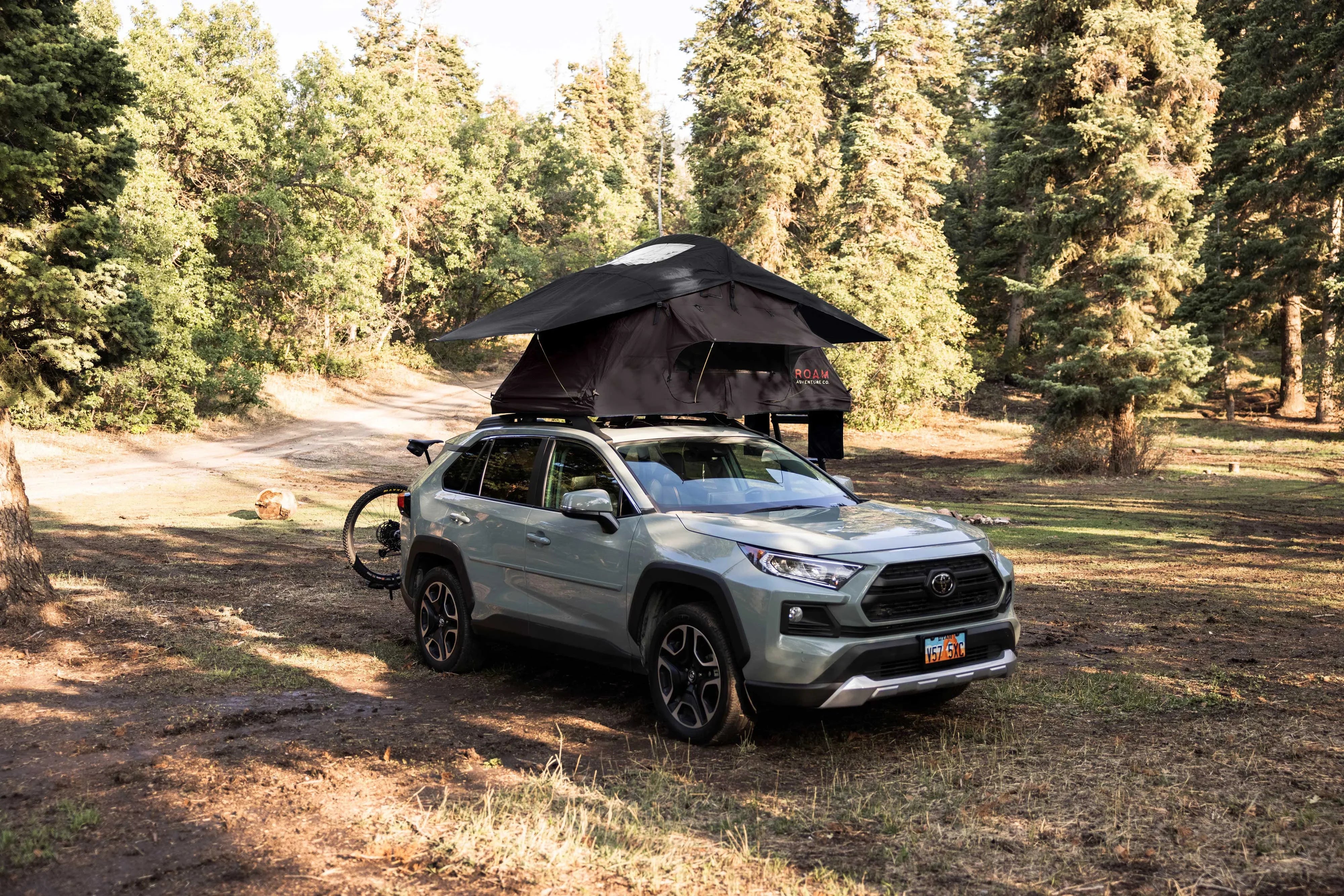 Toyota SUV with rooftop tent and bike rack parked in forest for overlanding and camping