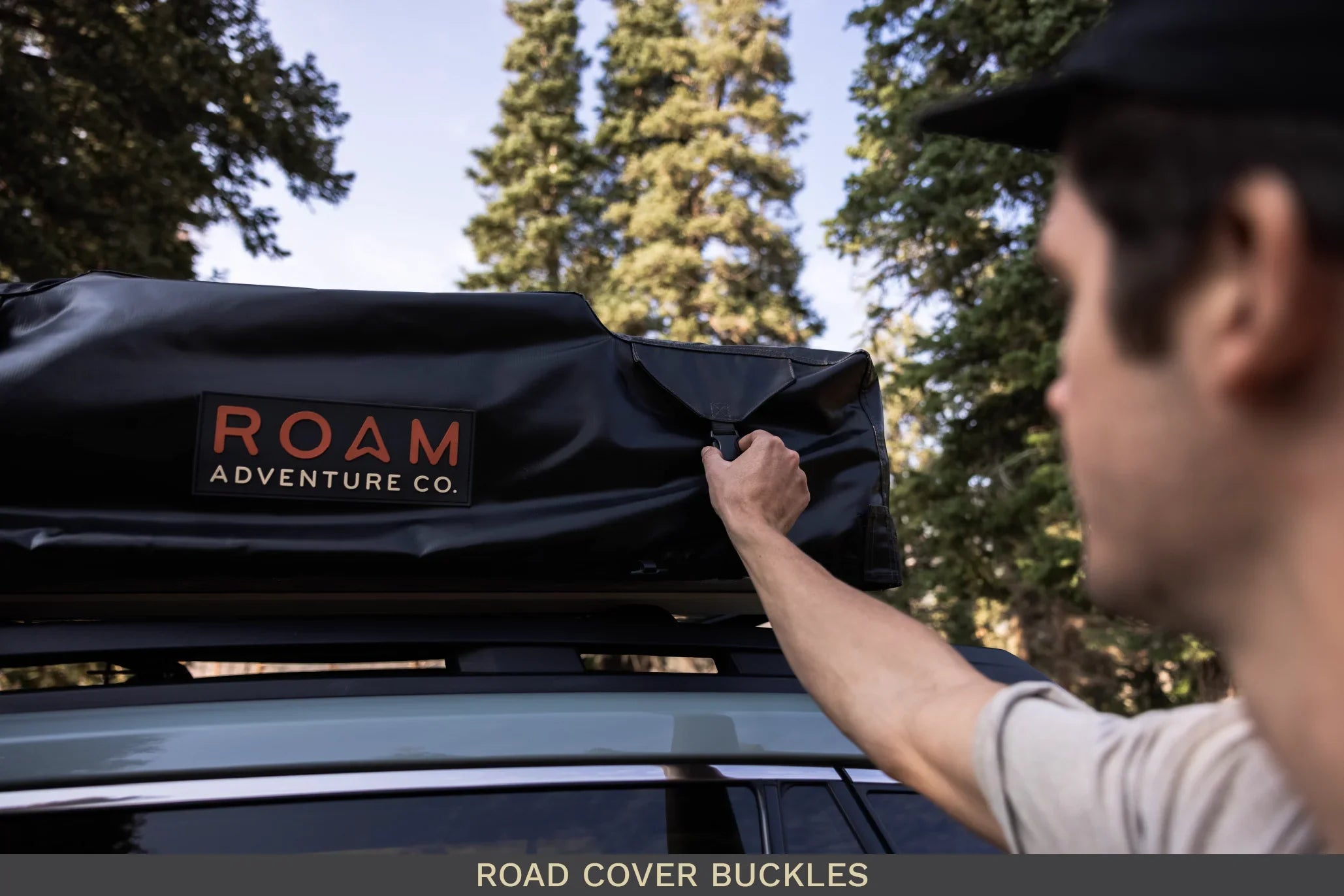 Man fastening buckle on rooftop tent cover mounted on vehicle for overlanding adventure