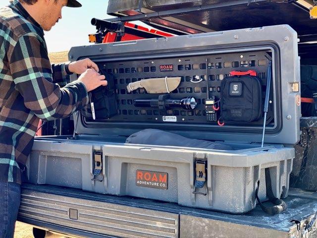 Man organizing overlanding gear in a ROAM storage case with MOLLE panel on a truck bed
