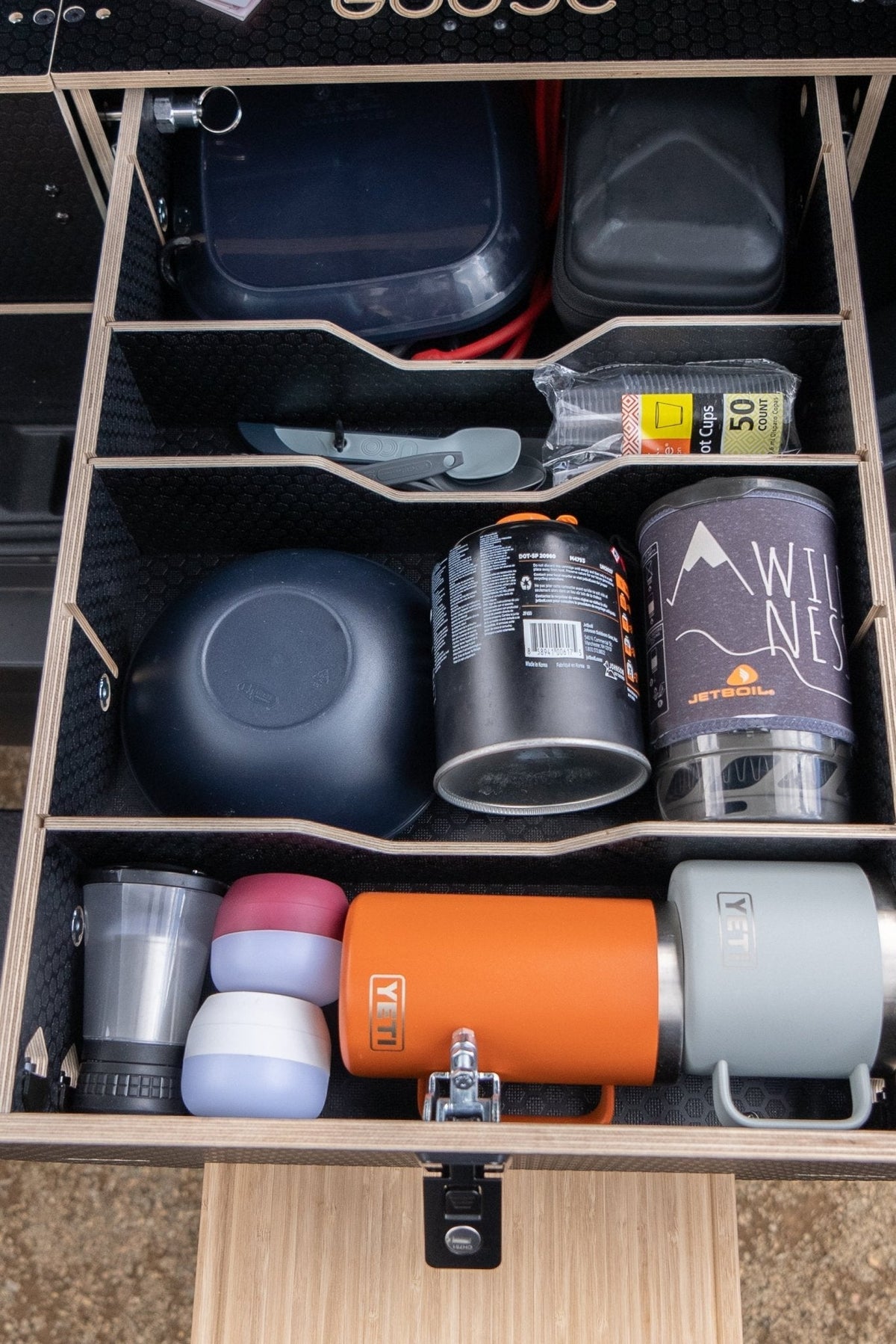 Inside a Goose Gear Park Series drawer with dividers, holding cookware, a stove canister, insulated mugs and an orange bottle