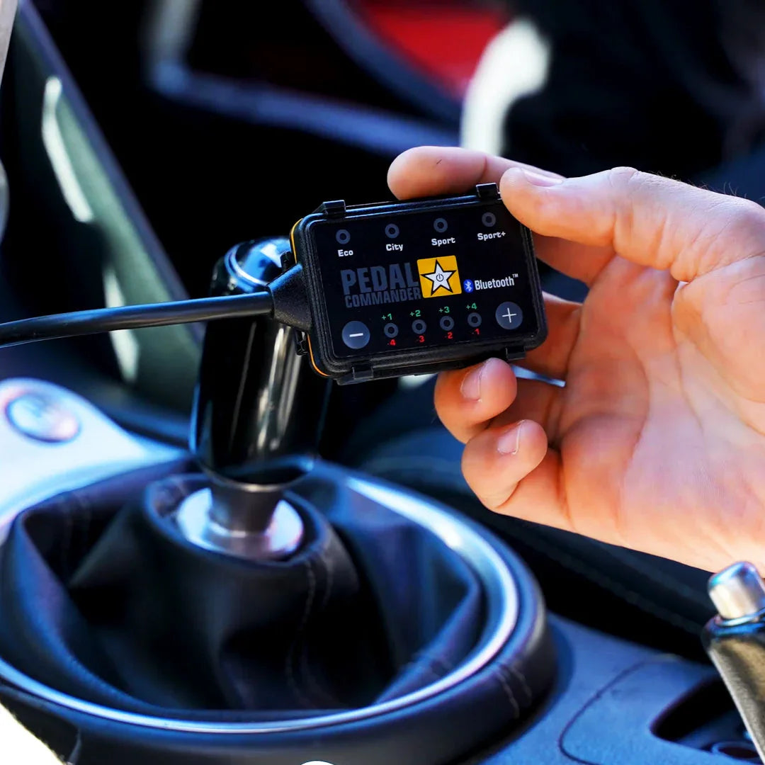 Hand holding Pedal Commander throttle controller in a car interior near manual gear shifter.