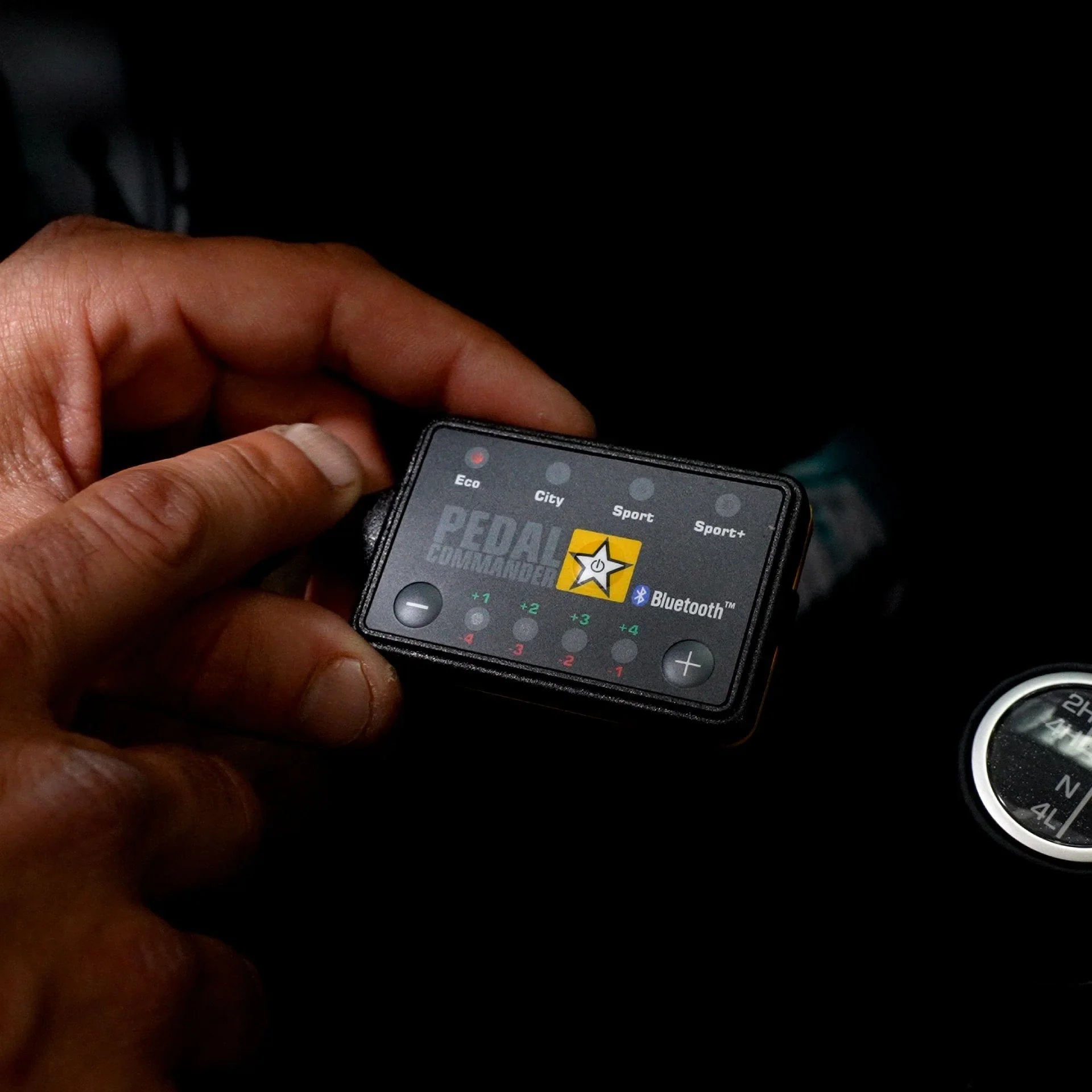Hand holding Pedal Commander throttle controller inside vehicle near gear shift knob.