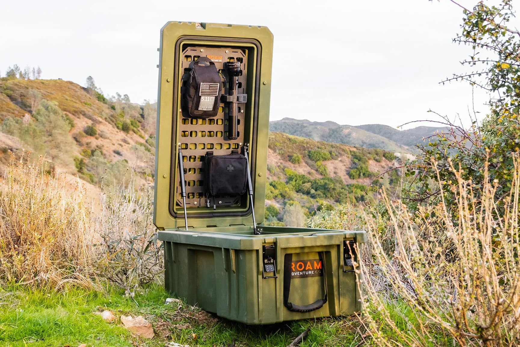 Outdoor adventure gear storage box with mounted organizer, set in rugged hillside terrain