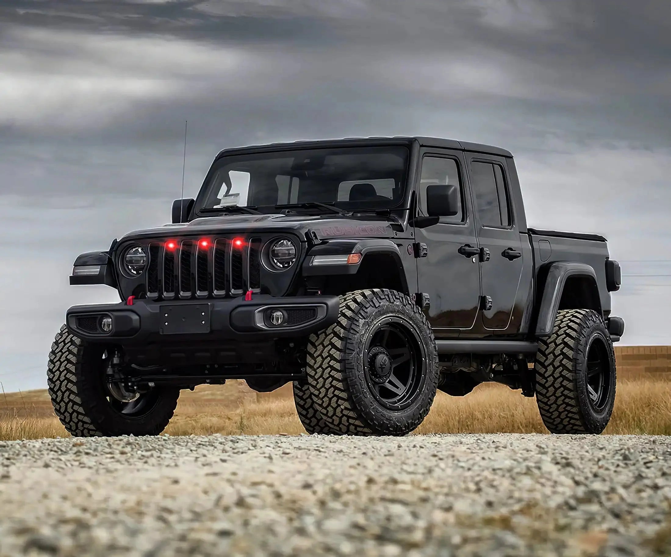 Black Jeep Gladiator Rubicon with large off-road tires and red grille lights on gravel