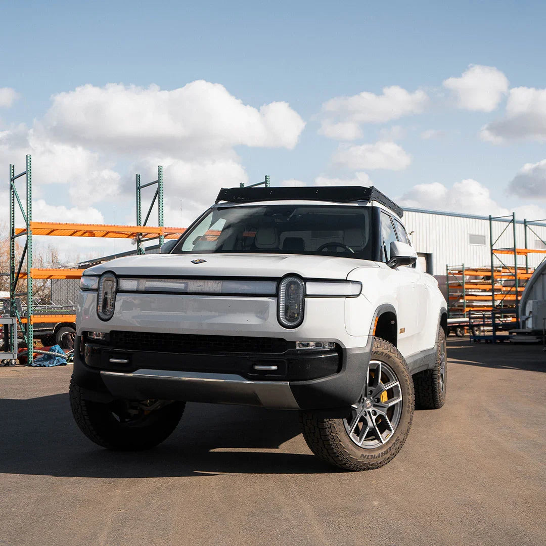 White Rivian R1T electric truck with off-road tires and roof rack in outdoor lot