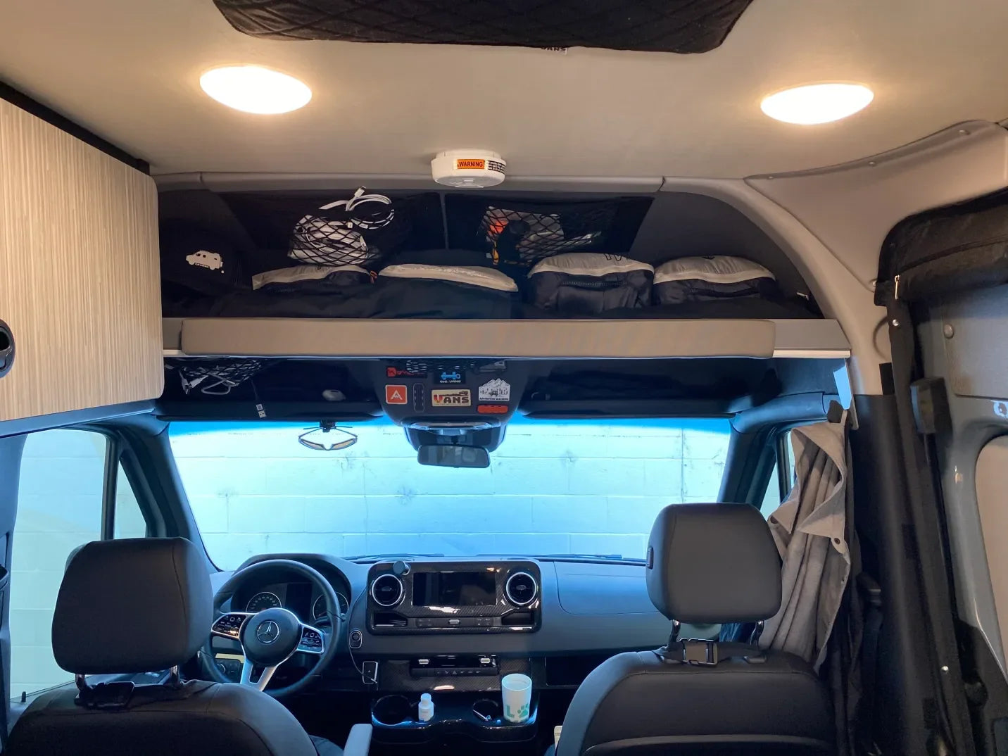 Interior of camper van with overhead storage shelf, camping gear, and modern dashboard