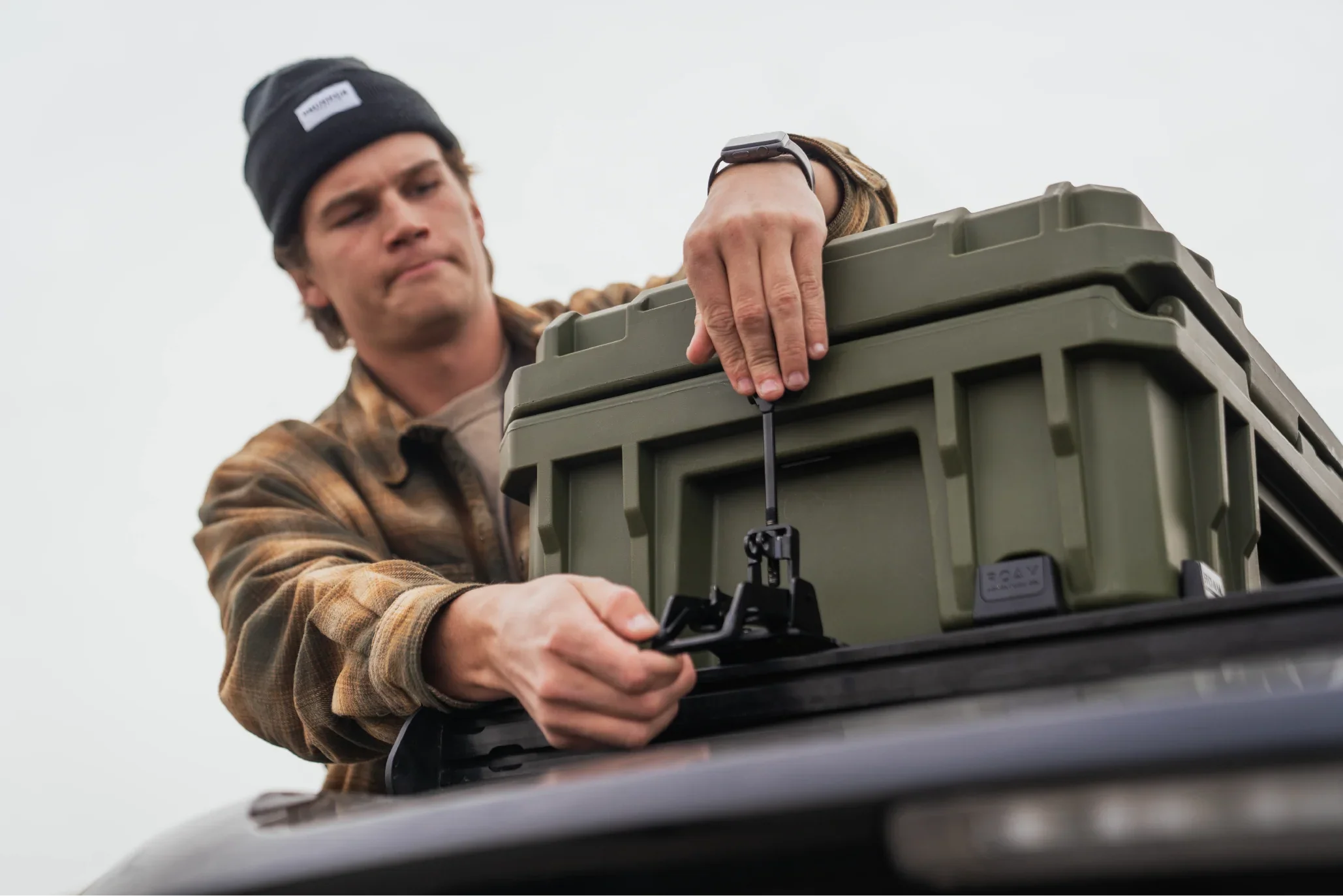 Man securing green storage case with rugged roof rack mount, overlanding gear setup