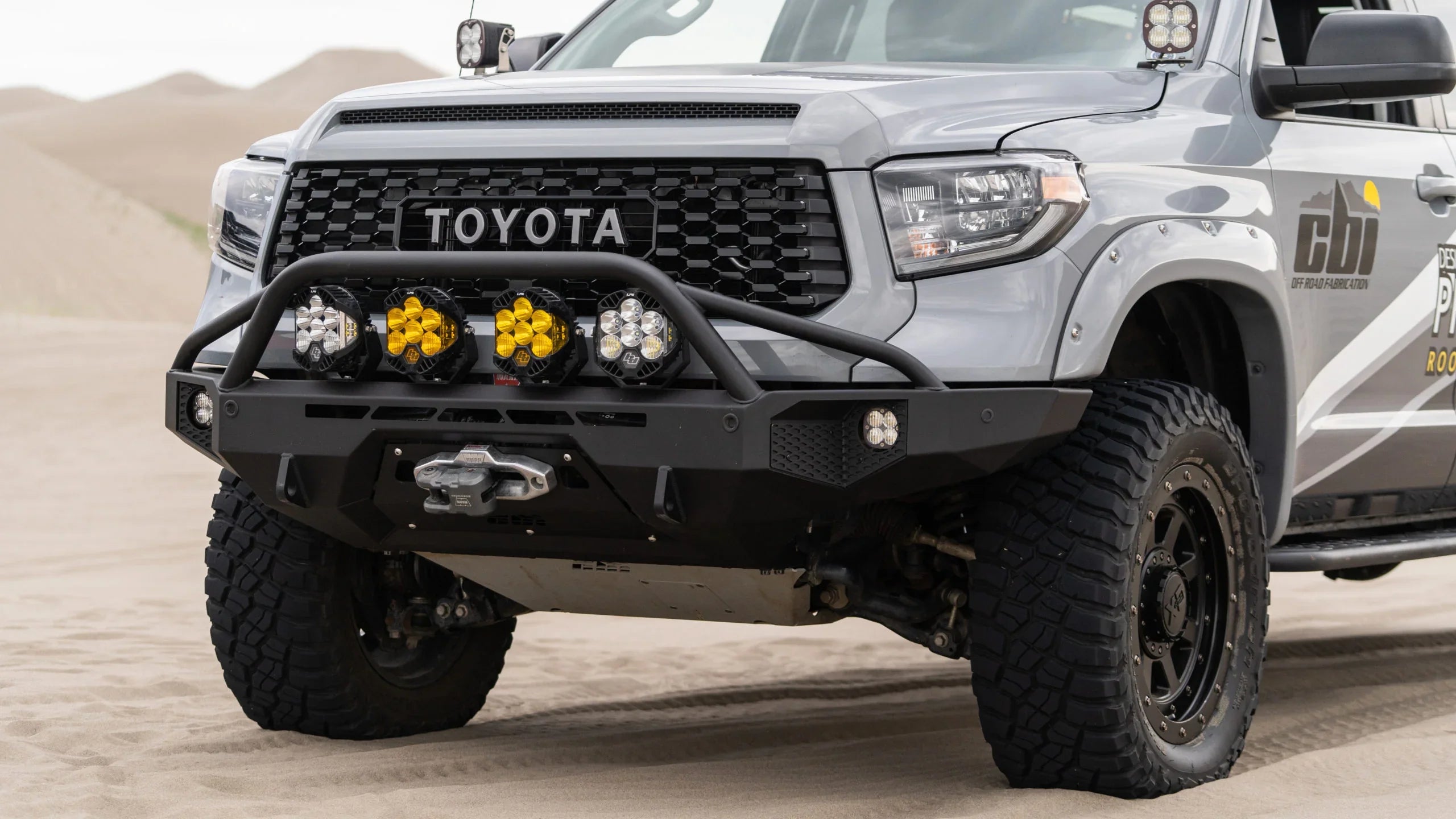 Toyota truck with off-road bumper, winch, and LED lights parked on sand dunes