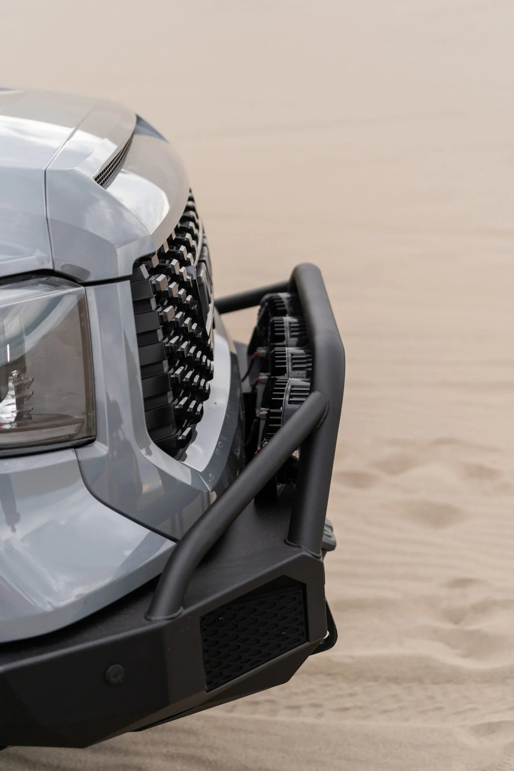 Close-up of off-road vehicle bumper with grille and LED lights on sand dunes