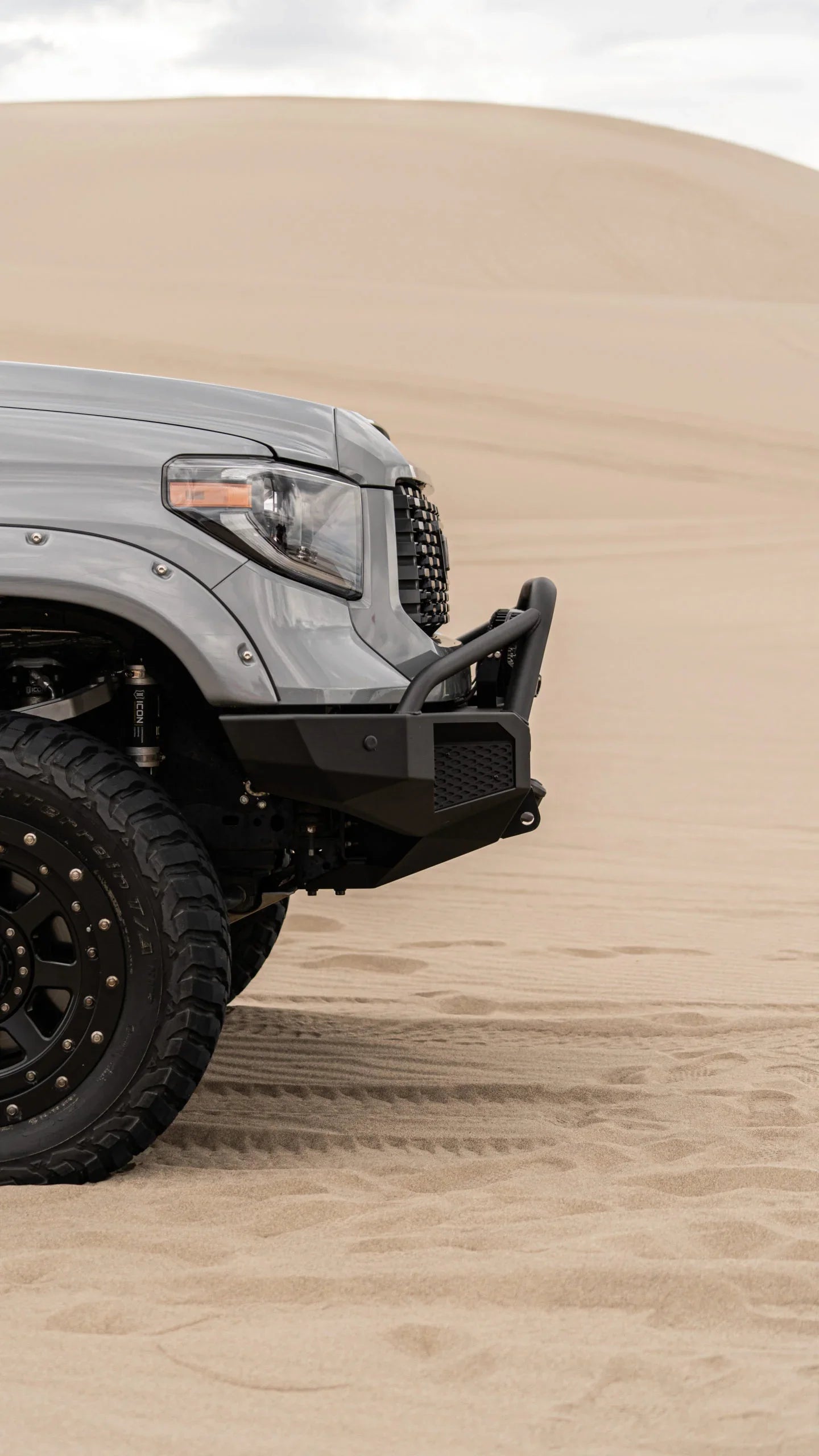 Off-road truck front with rugged bumper and all-terrain tire on sand dunes
