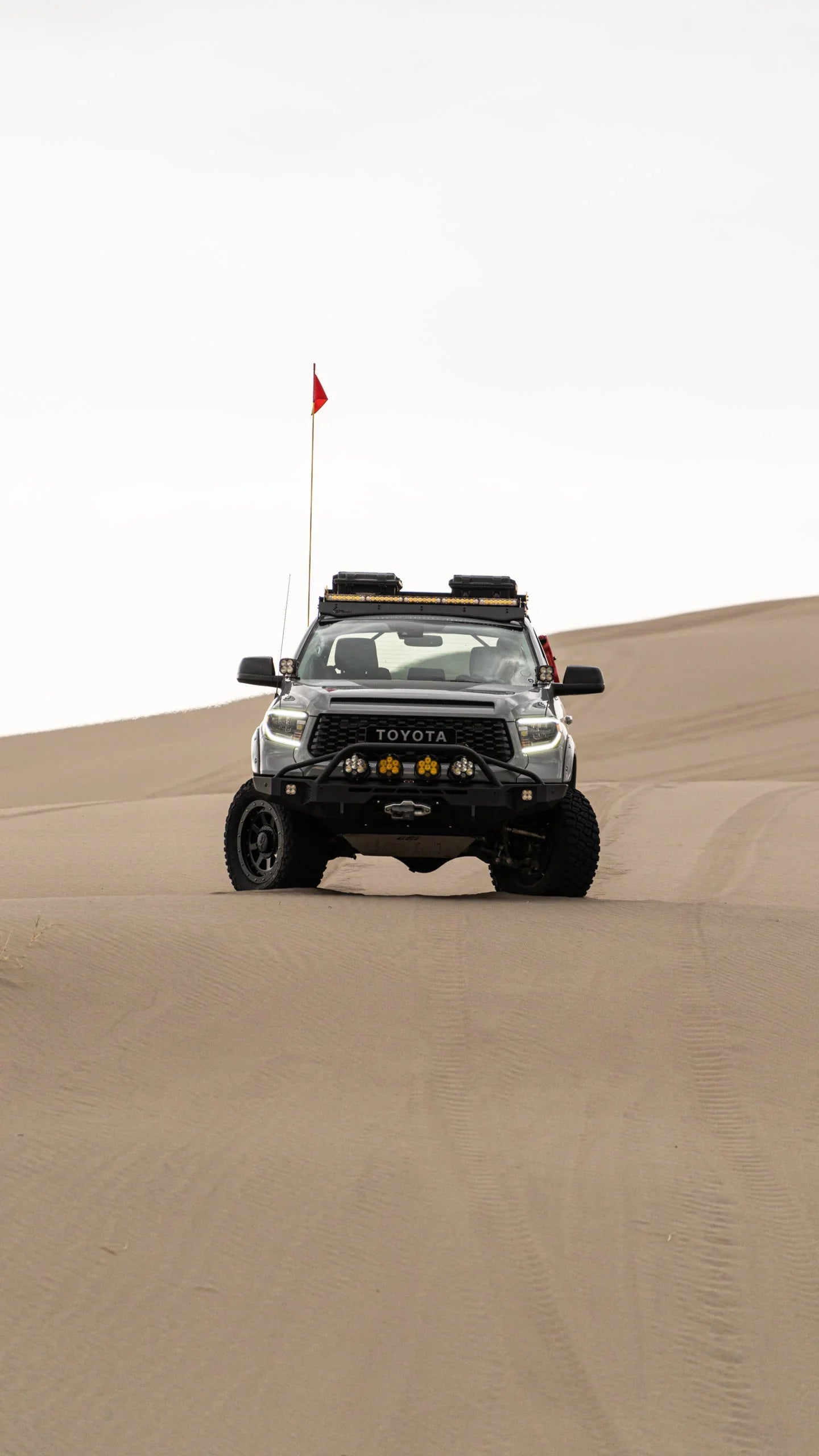 Toyota truck with overlanding gear driving on sand dunes in a desert landscape
