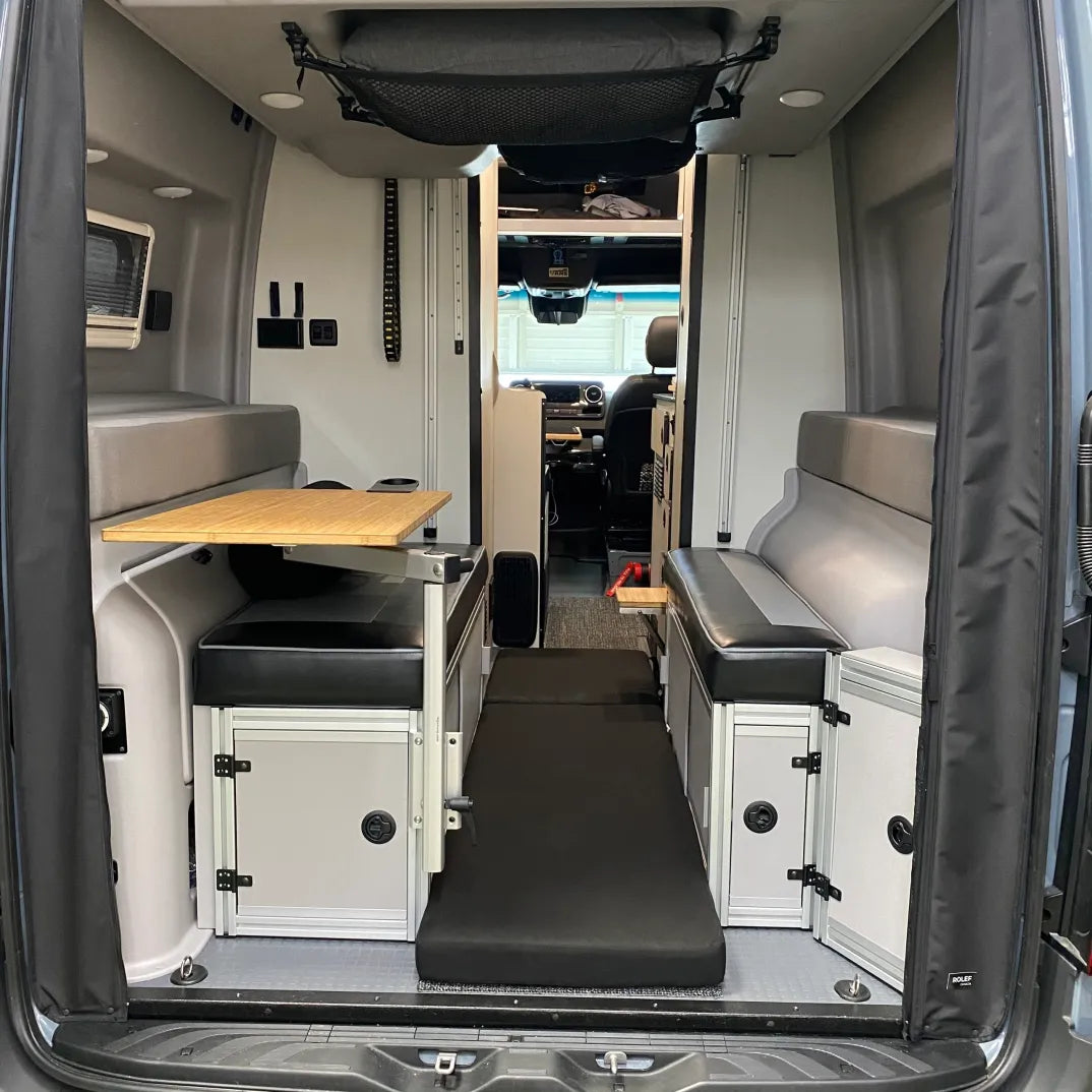 Overland camper van interior with folding table, storage cabinets, and bench seats