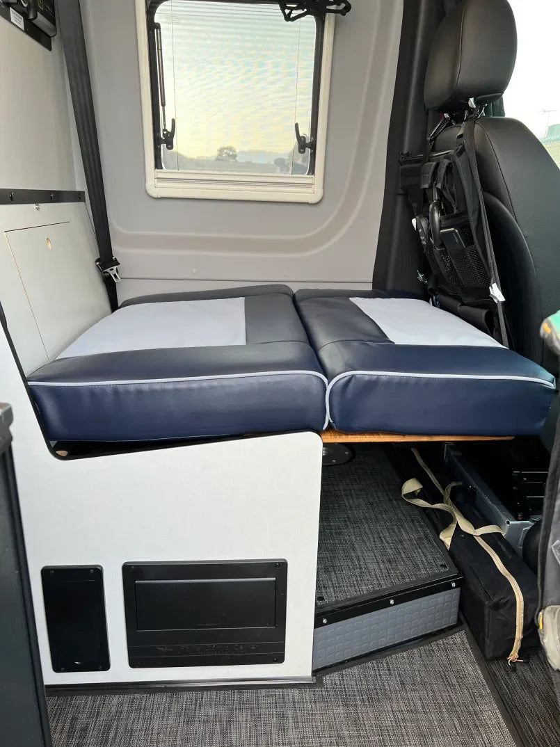 Overland vehicle camper interior with fold-out bed and window, ideal for adventure camping.