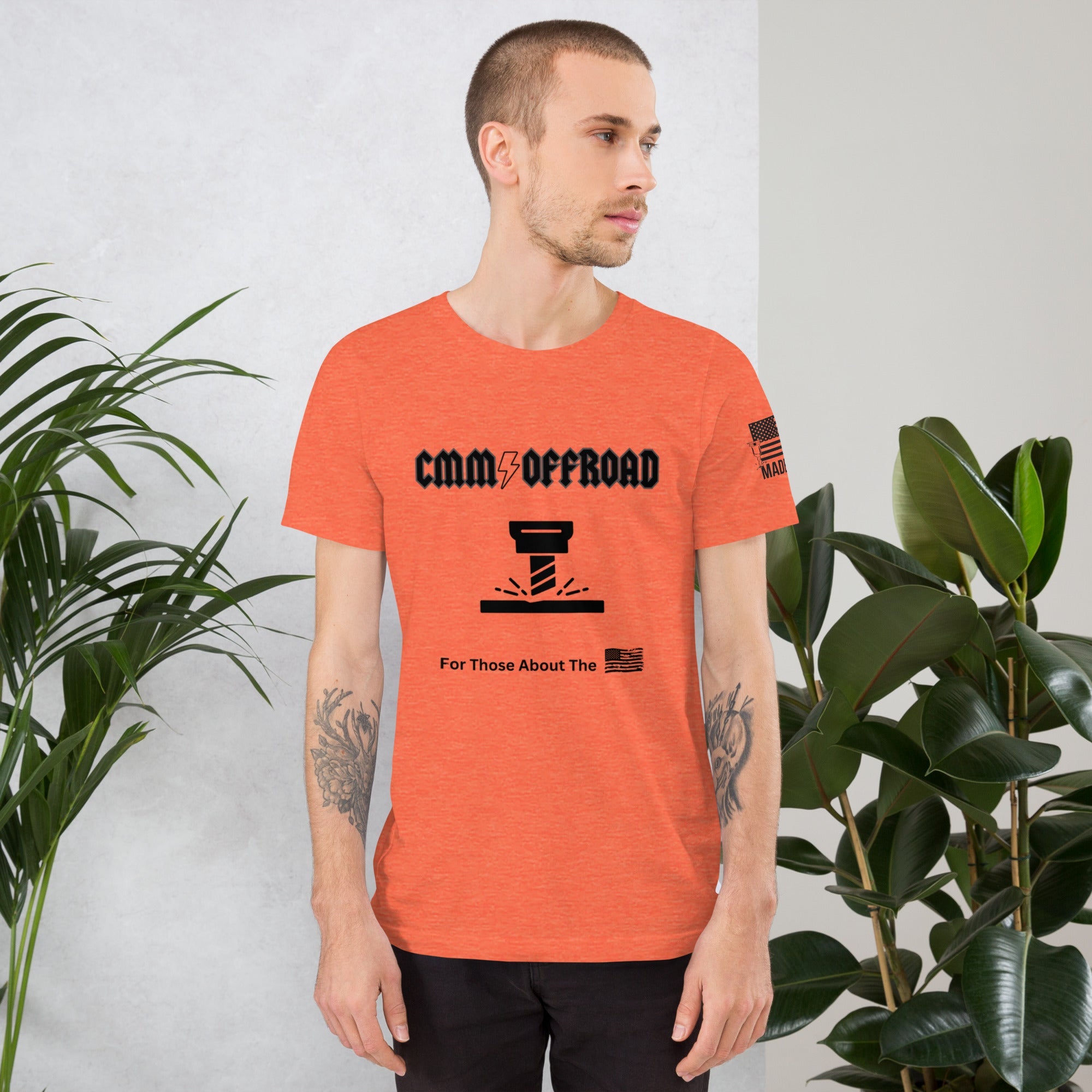 Man wearing heather orange CMM Offroad t-shirt with bolt graphic, standing near plants