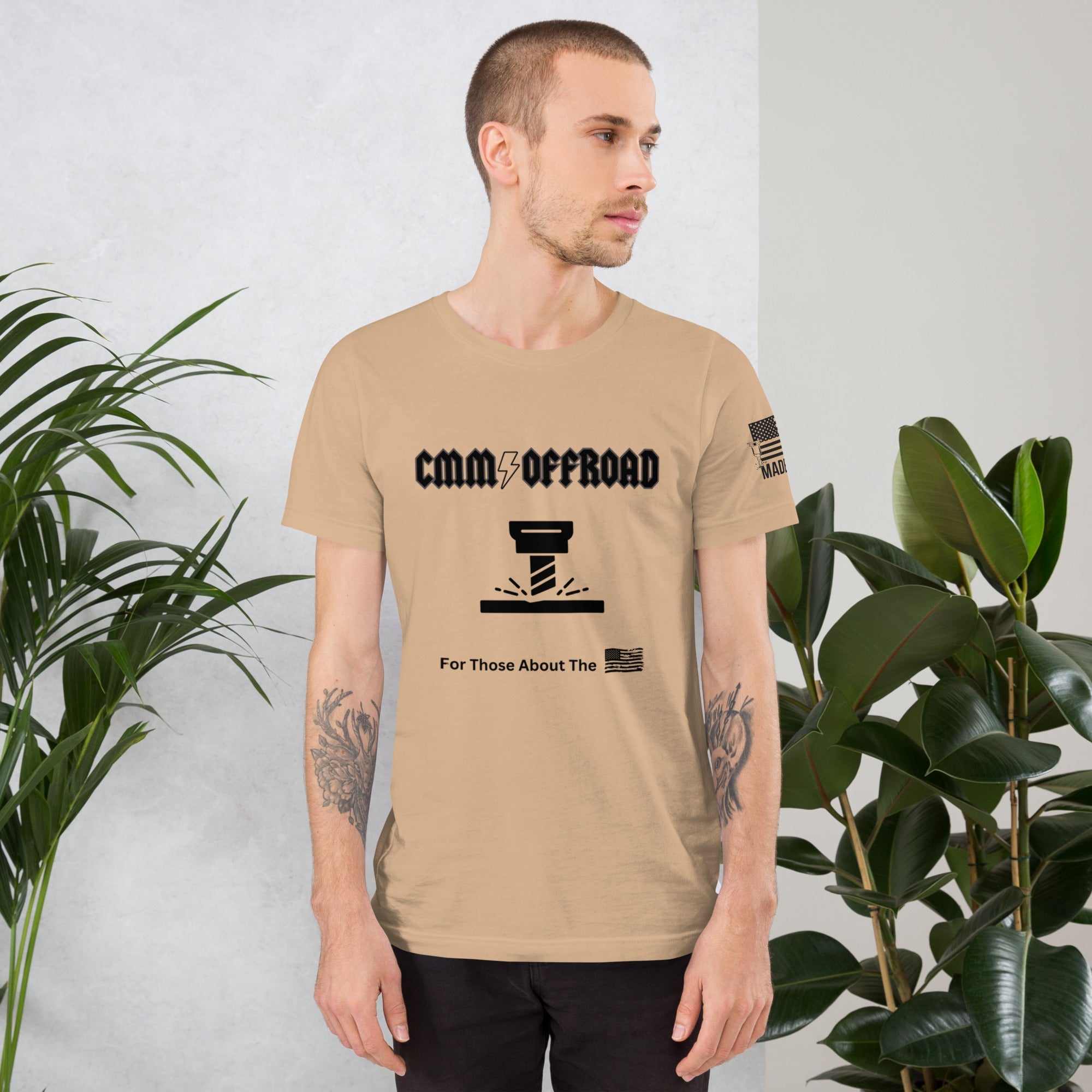 Man wearing tan unisex t-shirt with CMM Offroad graphic and American flag print, standing indoors