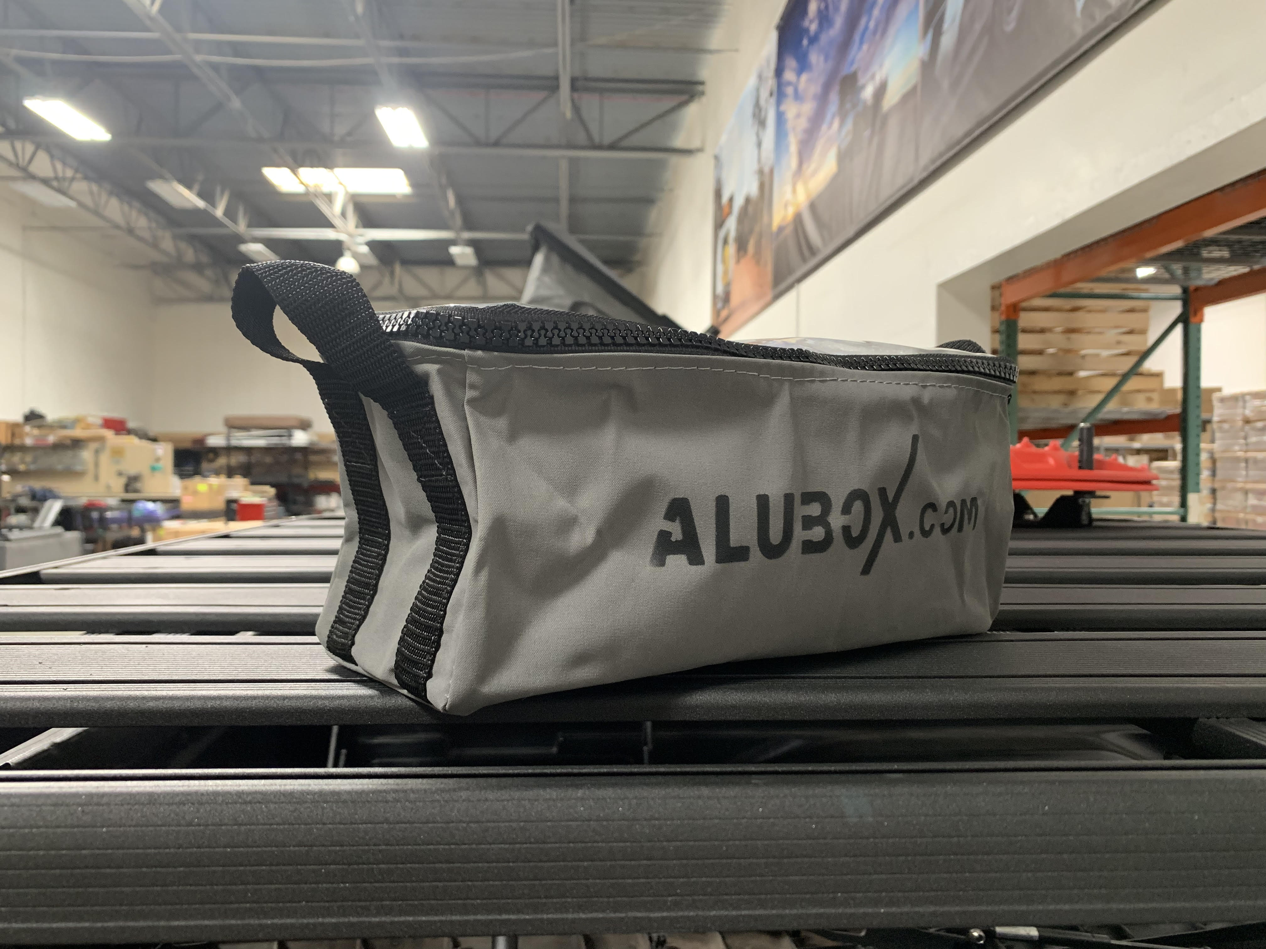 Alubox.com grey gear bag on a black roof rack in a warehouse, overlanding accessory