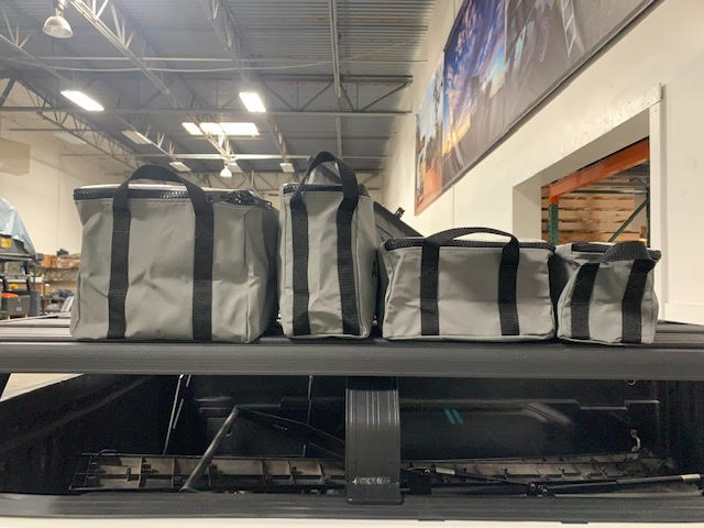 Set of gray and black overlanding gear storage bags on a truck bed in a warehouse