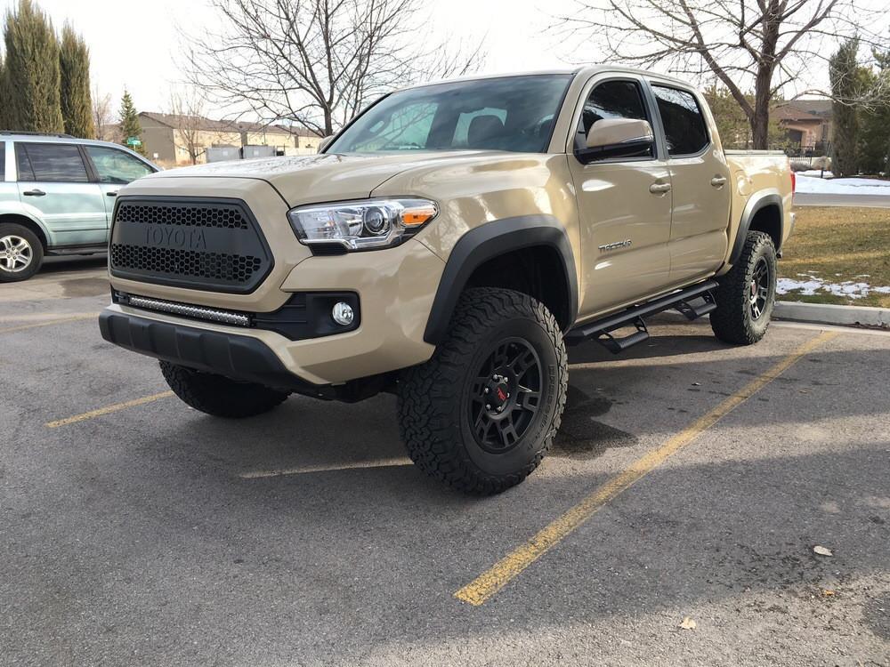 Lifted Toyota Tacoma with off-road tires and side steps parked outdoors in winter