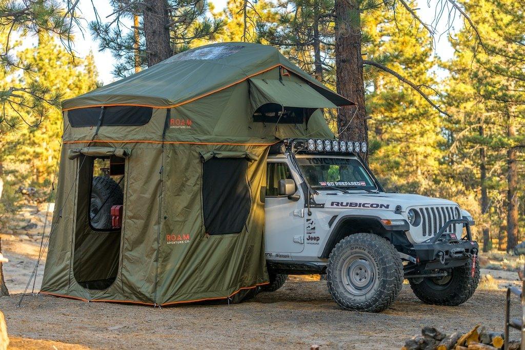 Overland rooftop tent mounted on Jeep Wrangler Rubicon in a forest campsite