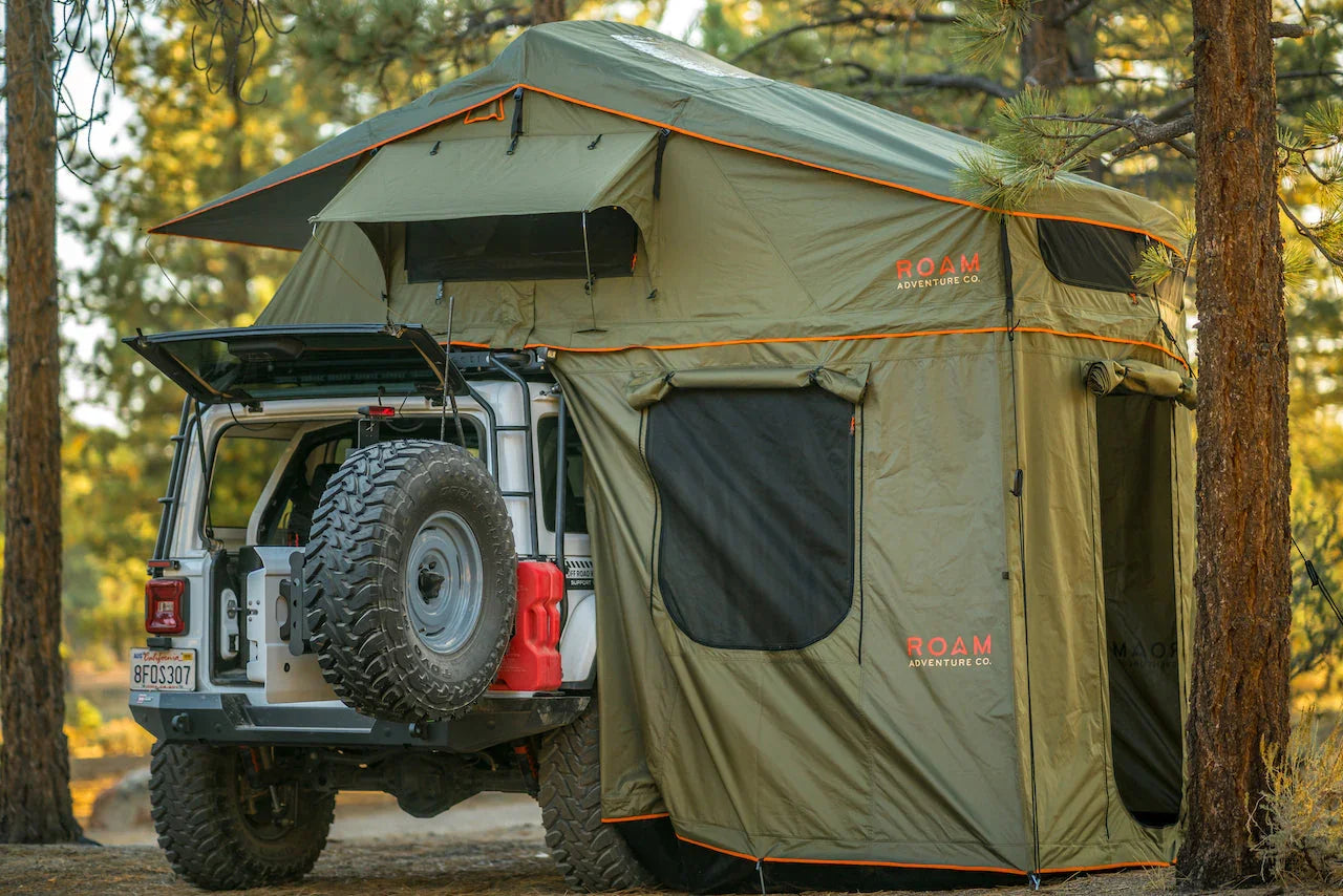 Jeep Gladiator with rooftop tent and annex set up for overlanding in a forest setting