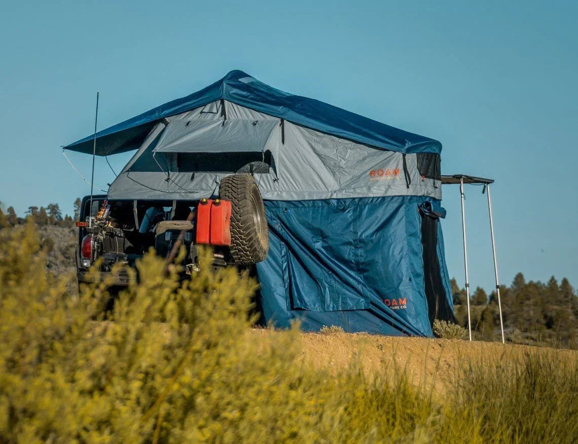 Overland vehicle with mounted rooftop tent and awning set up for camping outdoors