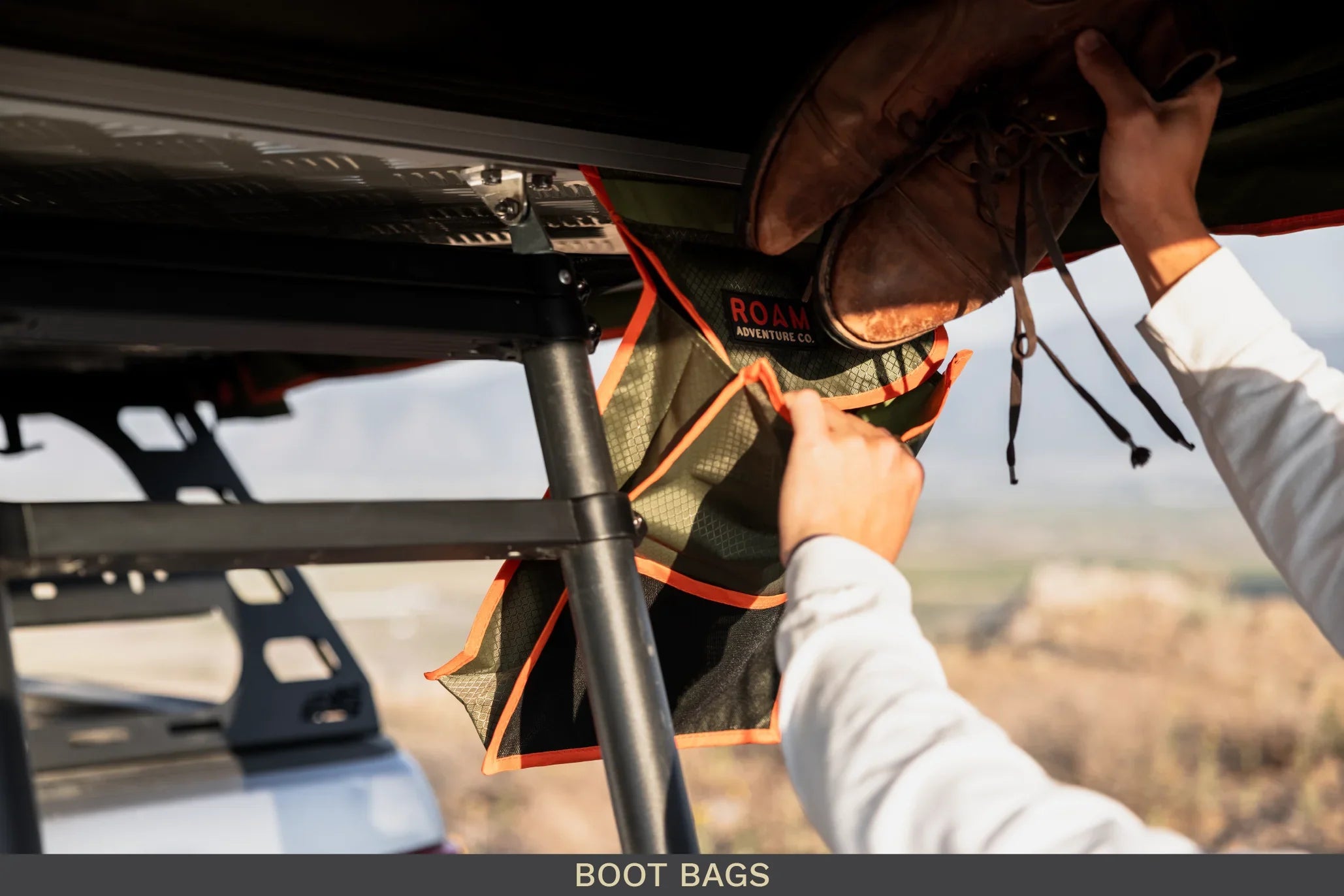 Attaching brown boots to an outdoor boot bag storage organizer on an overland vehicle rack.
