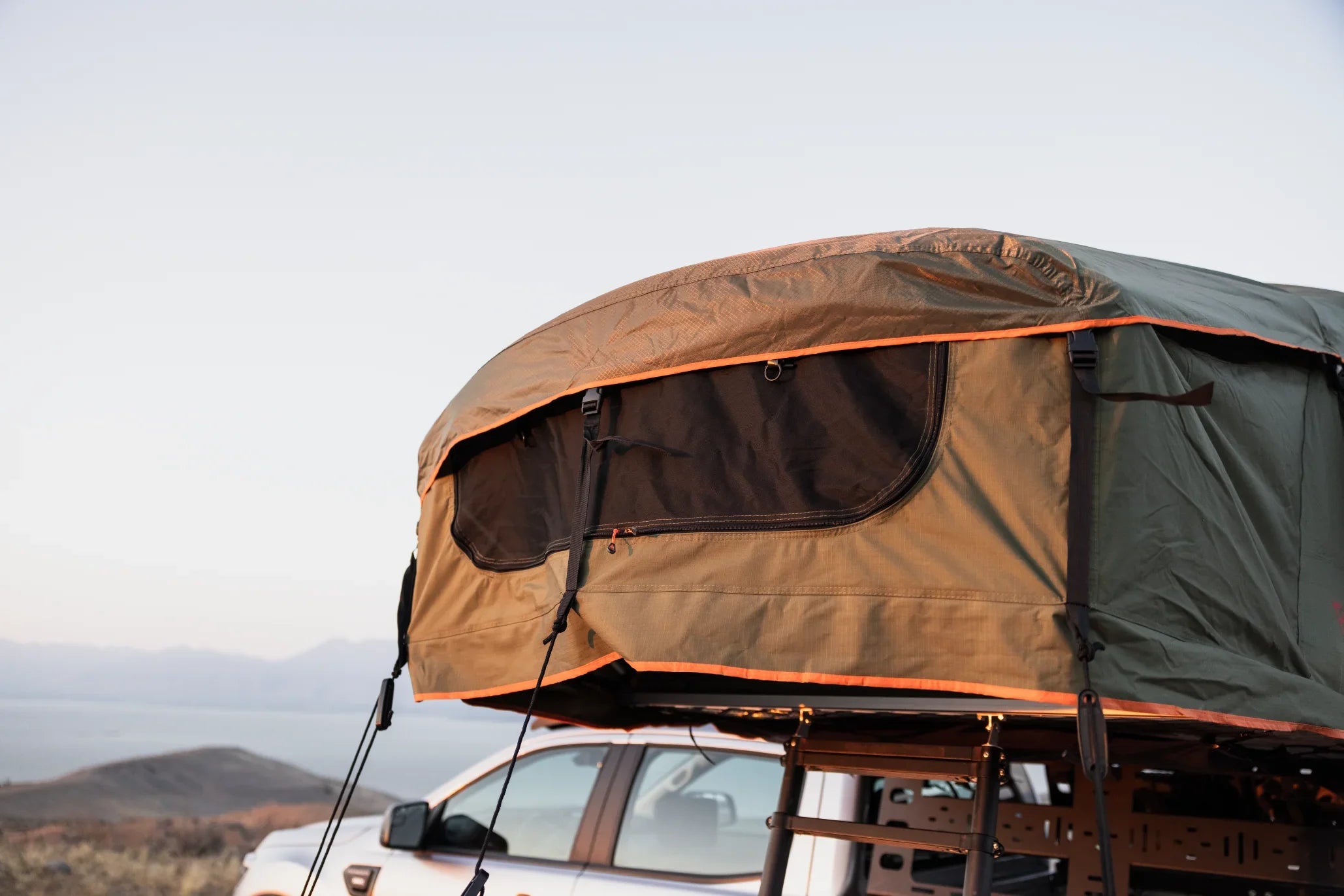 Rooftop tent mounted on a truck with outdoor camping gear, mountains in background