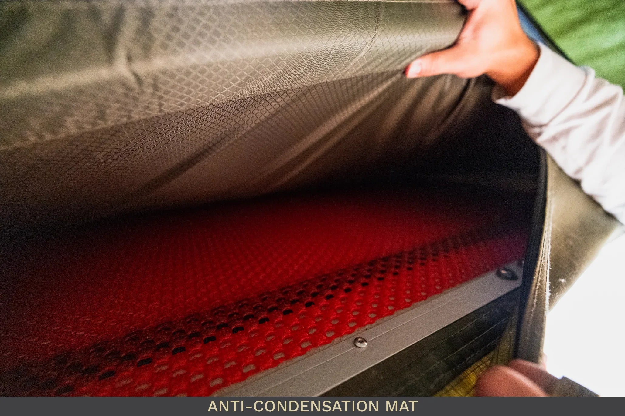Hand lifting tent mattress to reveal red anti-condensation mat for camping gear