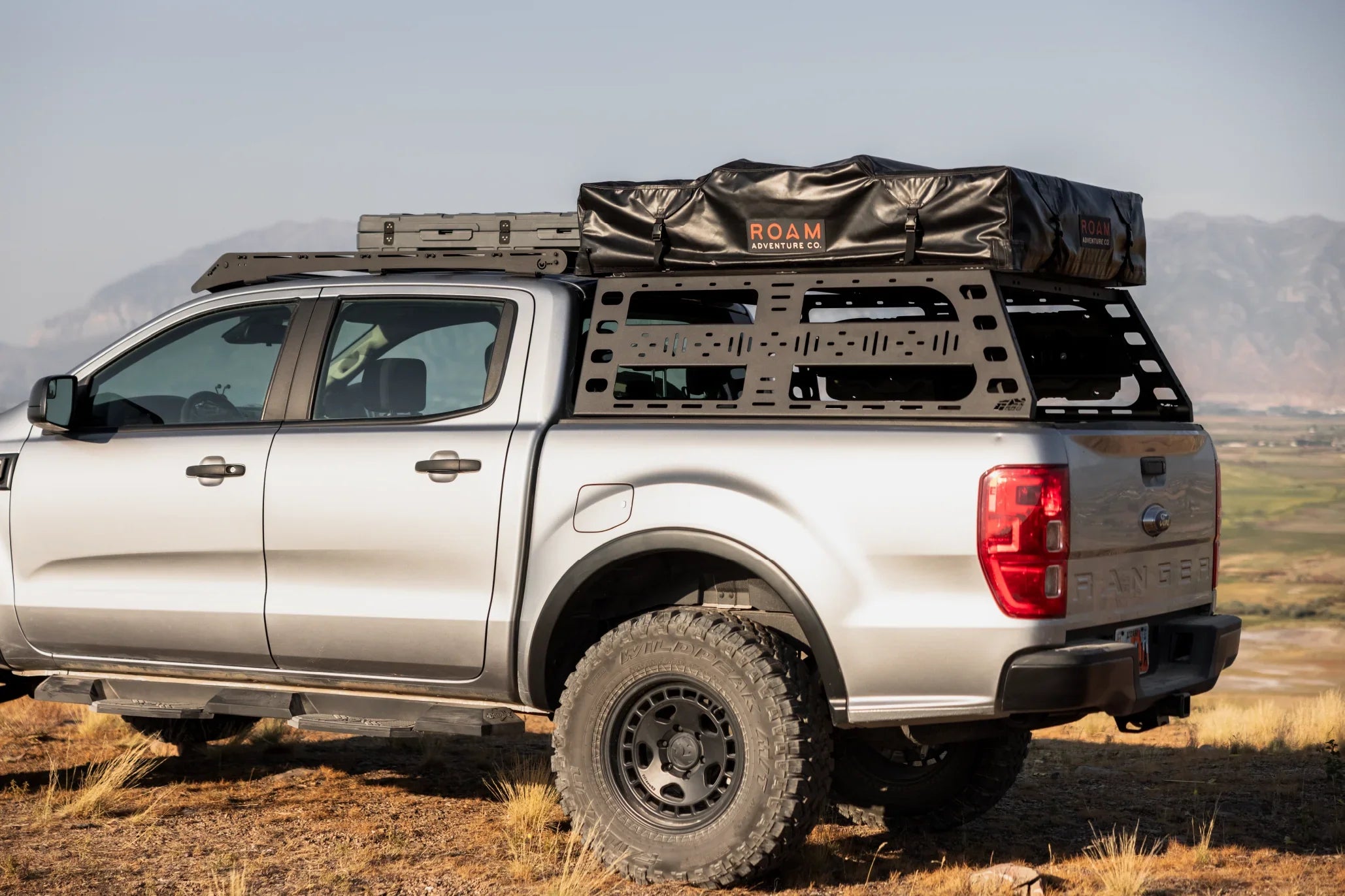 Silver off-road truck with overlanding rack and rooftop tent in outdoor setting