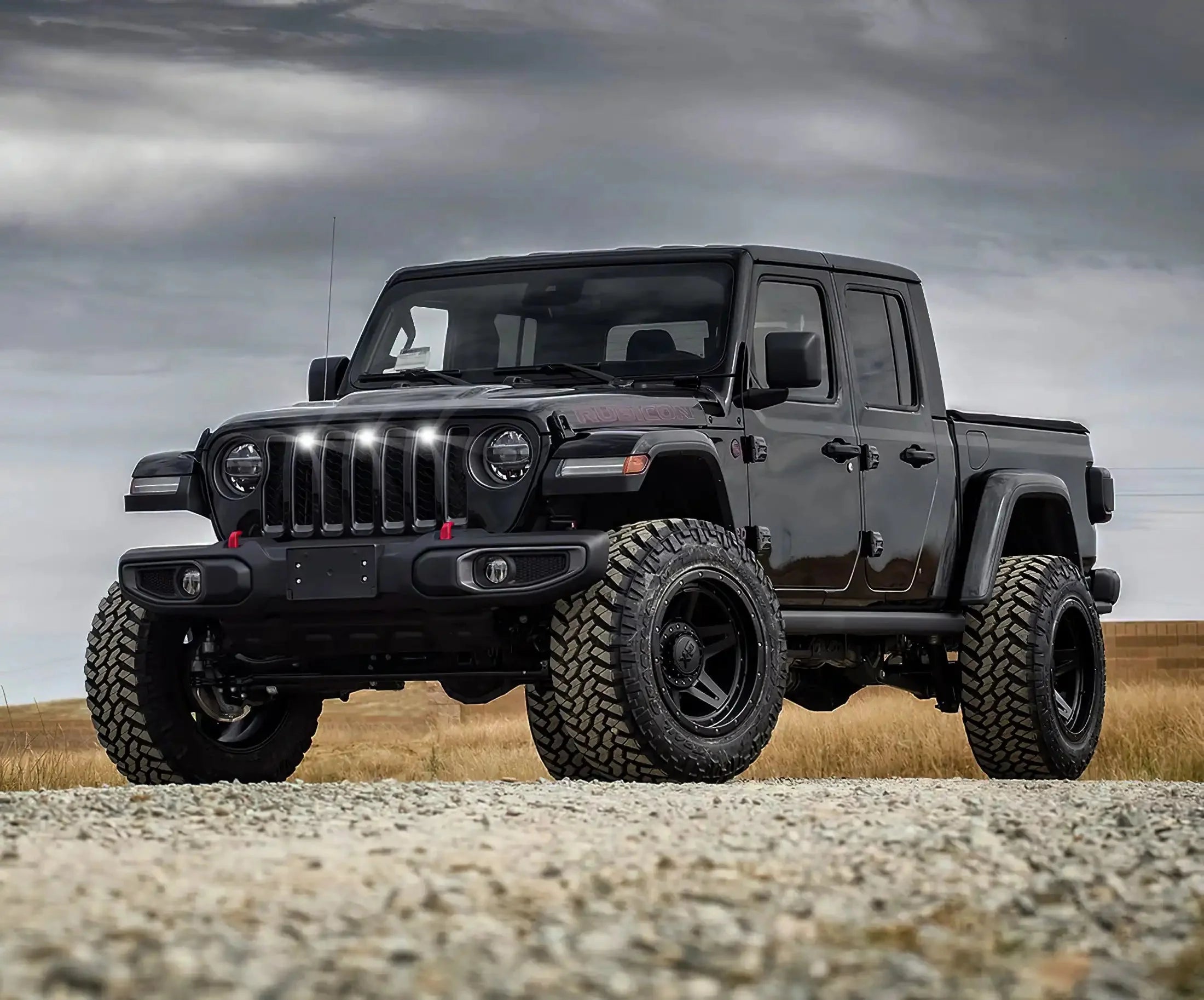 Black Jeep Gladiator Rubicon with off-road tires on gravel road under cloudy sky