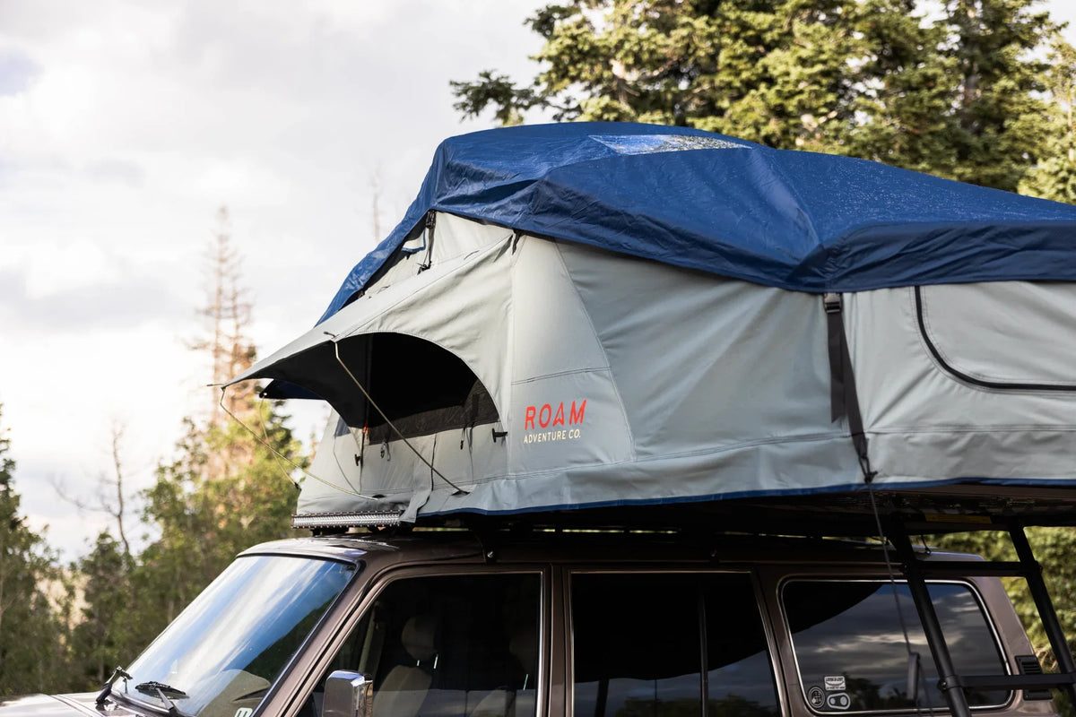 Overland roof top tent with rainfly set up on vehicle for camping in the forest