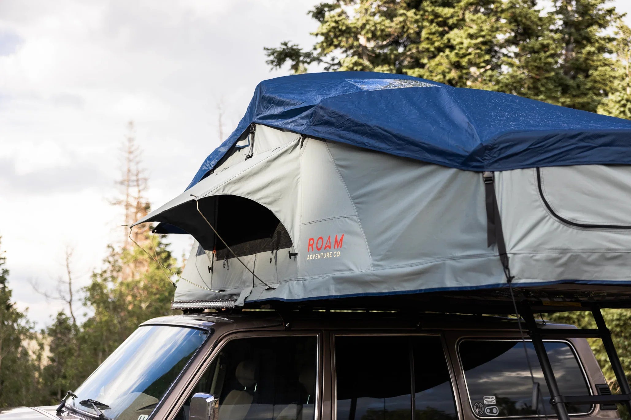 Overland roof top tent with rainfly set up on vehicle for camping in the forest