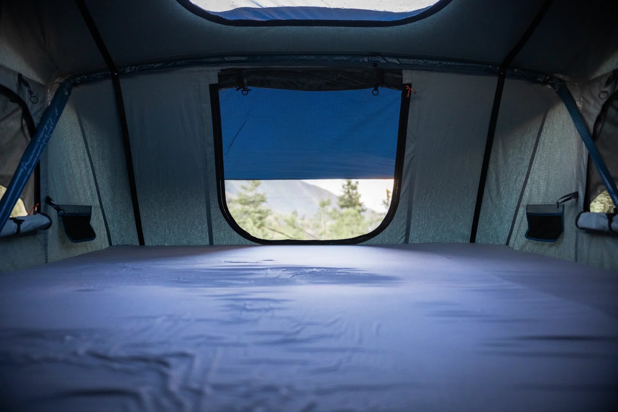 Interior view of rooftop tent with window overlooking outdoor forest and mountains