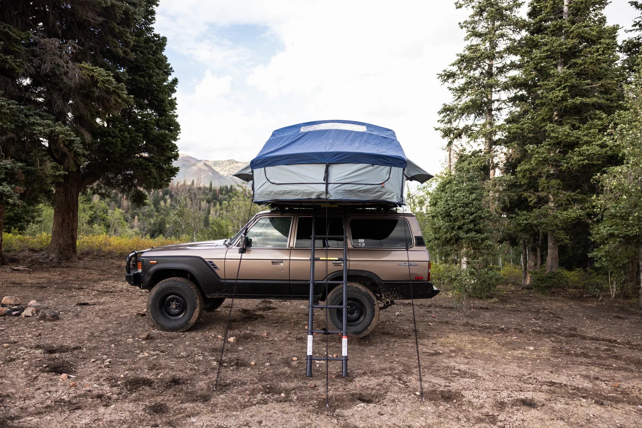 SUV with a rooftop tent set up for overlanding in a forested camping area