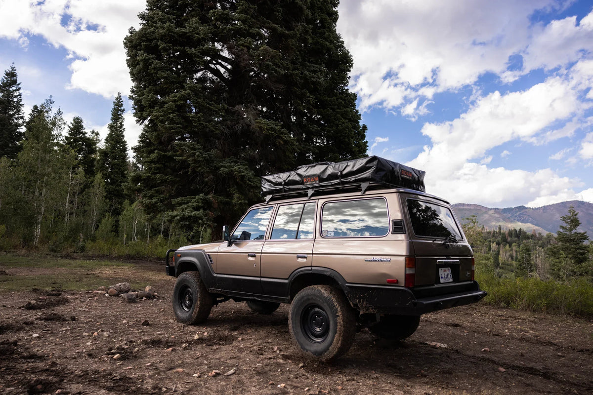 Classic SUV with rooftop tent parked in forest, ideal for overlanding and camping