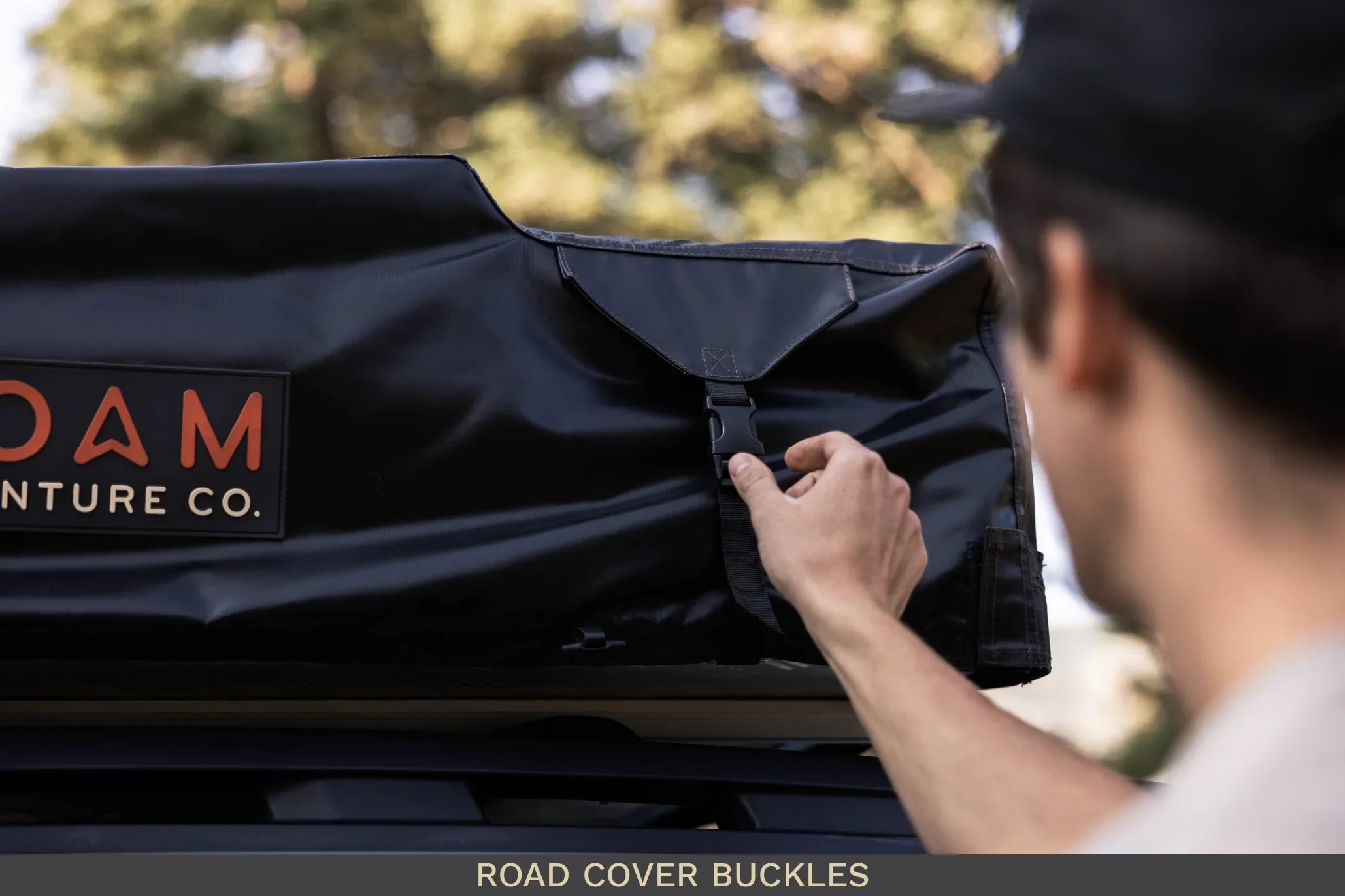 Person fastening buckle on rooftop tent cover for overlanding vehicle outdoors