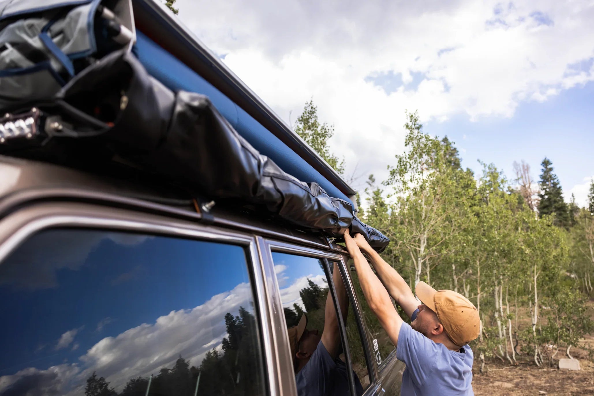 Setting up vehicle rooftop awning for camping outdoors in forested area